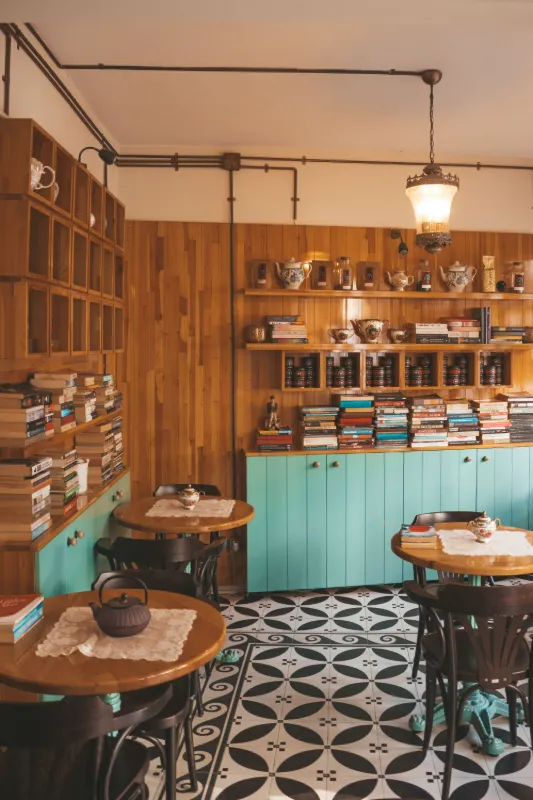 Ahşap duvarlı, kitaplı ve turkuaz dolaplı sıcak bir kafe salonu